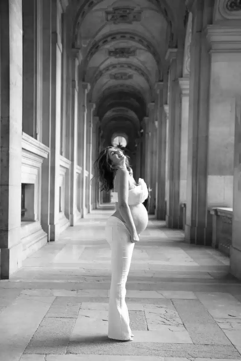 Sandra Da Silva enceinte, maman à 40 ans, en ensemble blanc dans une galerie du Louvre, photo grossesse noir et blanc